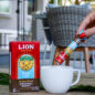 Lion Coffee Box of Instant Coffee Sticks - Original Roast, with hand pouring instant coffee into a mug