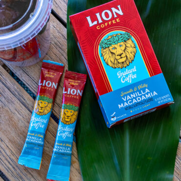 Lion Vanilla Macadamia Instant Coffee Box with two instant coffee sticks on top of a green leaf