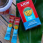 Lion Vanilla Macadamia Instant Coffee Box with two instant coffee sticks on top of a green leaf